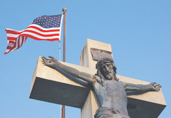 The American flag flies near the crucifix in the cemetery at St. Vincent de Paul Parish in Shelby County. During Memorial Day weekend liturgies, Catholics remember deceased loved ones and veterans who died in service to our country. (Photo by Mary Ann Wyand)