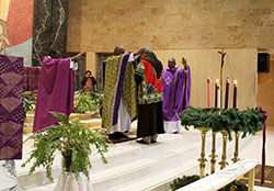 Wearing an African shirt that was a gift from the members of the archdiocesan African Catholic Ministry, Franciscan Brother Moises Gutierrez is blessed by Father Kenneth Taylor, pastor of St. Rita and Holy Angels parishes, at St. Rita Church in Indianapolis on Dec. 6. Also participating in the blessing are Fathers John Kamwendo, associate pastor of St. Pius X Parish in Indianapolis, left, and Immanuel Nyong, a chaplain at IU Health Methodist Hospital in Indianapolis. (Photo by Victoria Arthur)