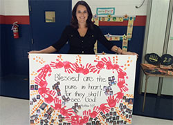 Brittany Geswein holds a canvas that captures her favorite Beatitude and the photos of her students—past and present—at St. Mary-of-the-Knobs School. (Submitted photo) 